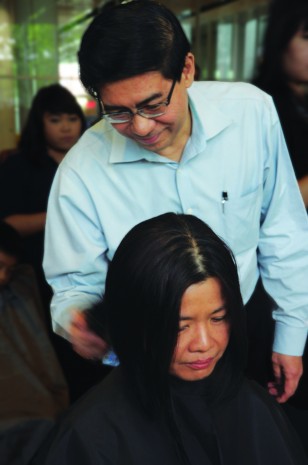 BEFORE THE CUT: Principal/CEO Yeo Li Pheow lending a hand at the event. Here he is cutting facilitator Cecilia Ow’s hair. (Photo: Valerie Priya)