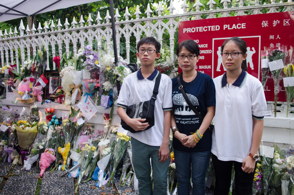 A LESSON FOR ALL: (From left) Ming Yang, Jean Er and Wei Lin stand in front of a row of gifts left by the mourning visitors. Jean wanted to teach her  children something about Mr Lee, so she decided to bring both of  them down to the Istana on Tuesday, where Mr Lee lay inside during a private wake. The trio wrote condolence cards and left a bunch of flowers. (Photo: Marcus Tan)